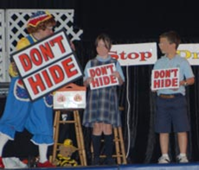 Rainbow and two children hold signs that say "Don't Hide"
