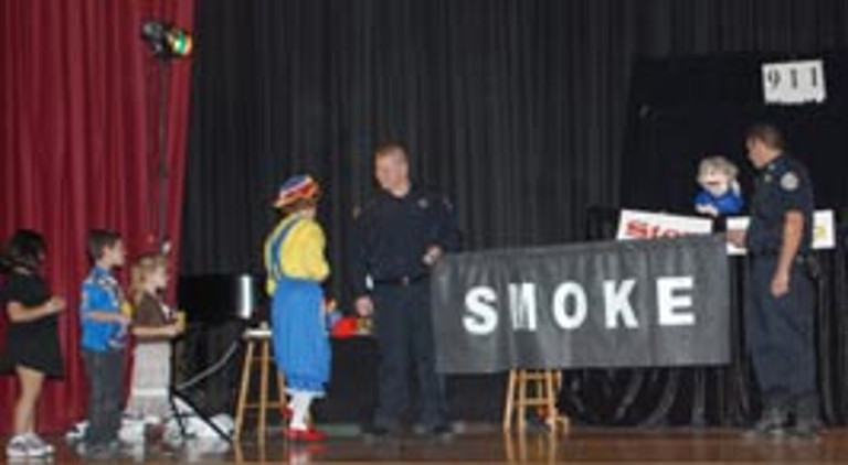 Rainbow talks to a fire fighter holding a banner that reads "smoke"